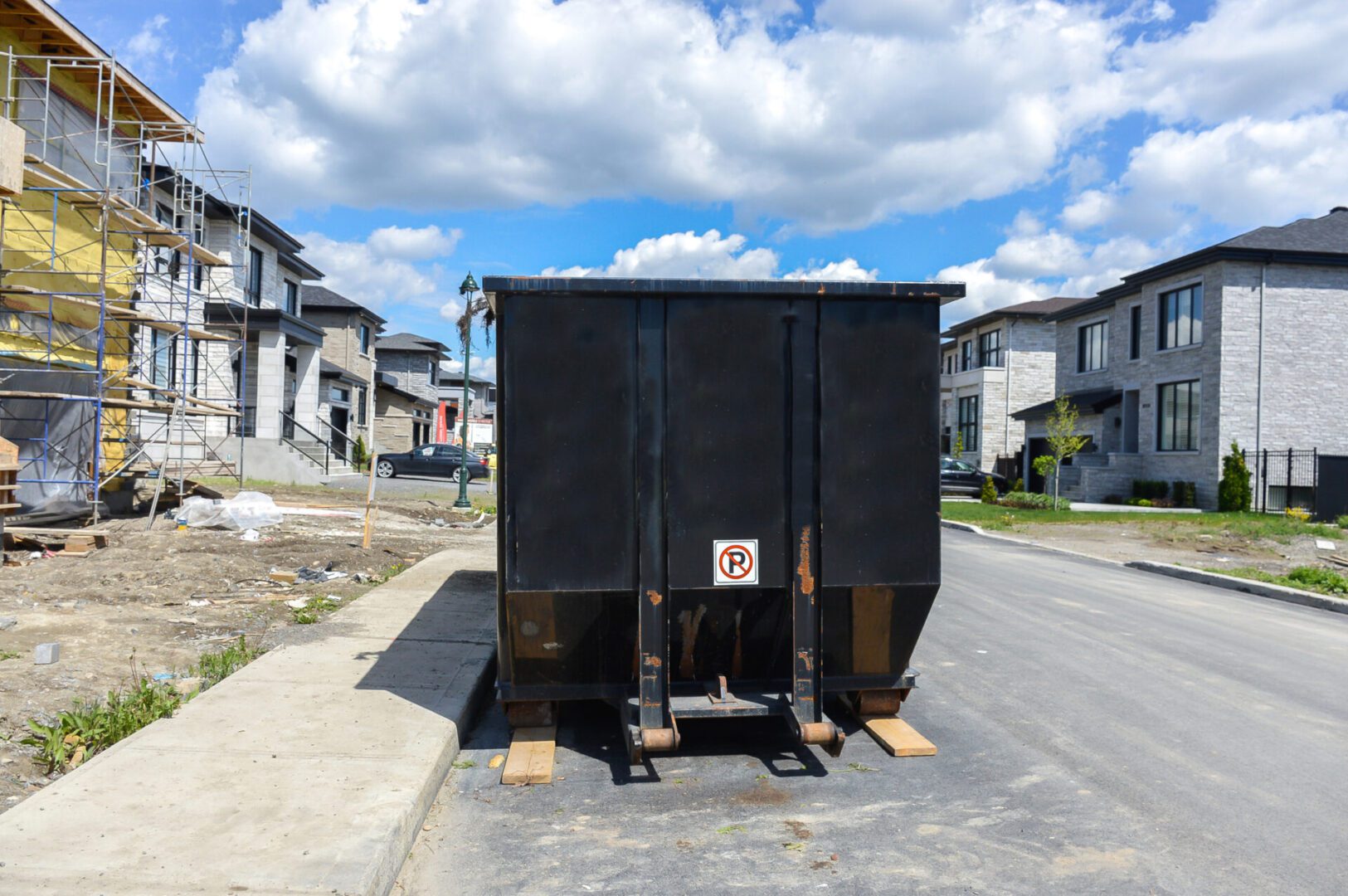 A large black dumpster on a residential street under a blue sky.