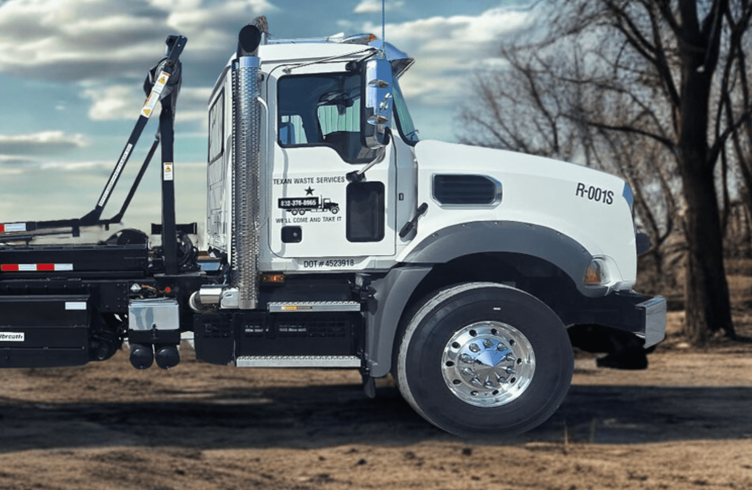 White heavy-duty truck parked on dirt ground under cloudy sky.