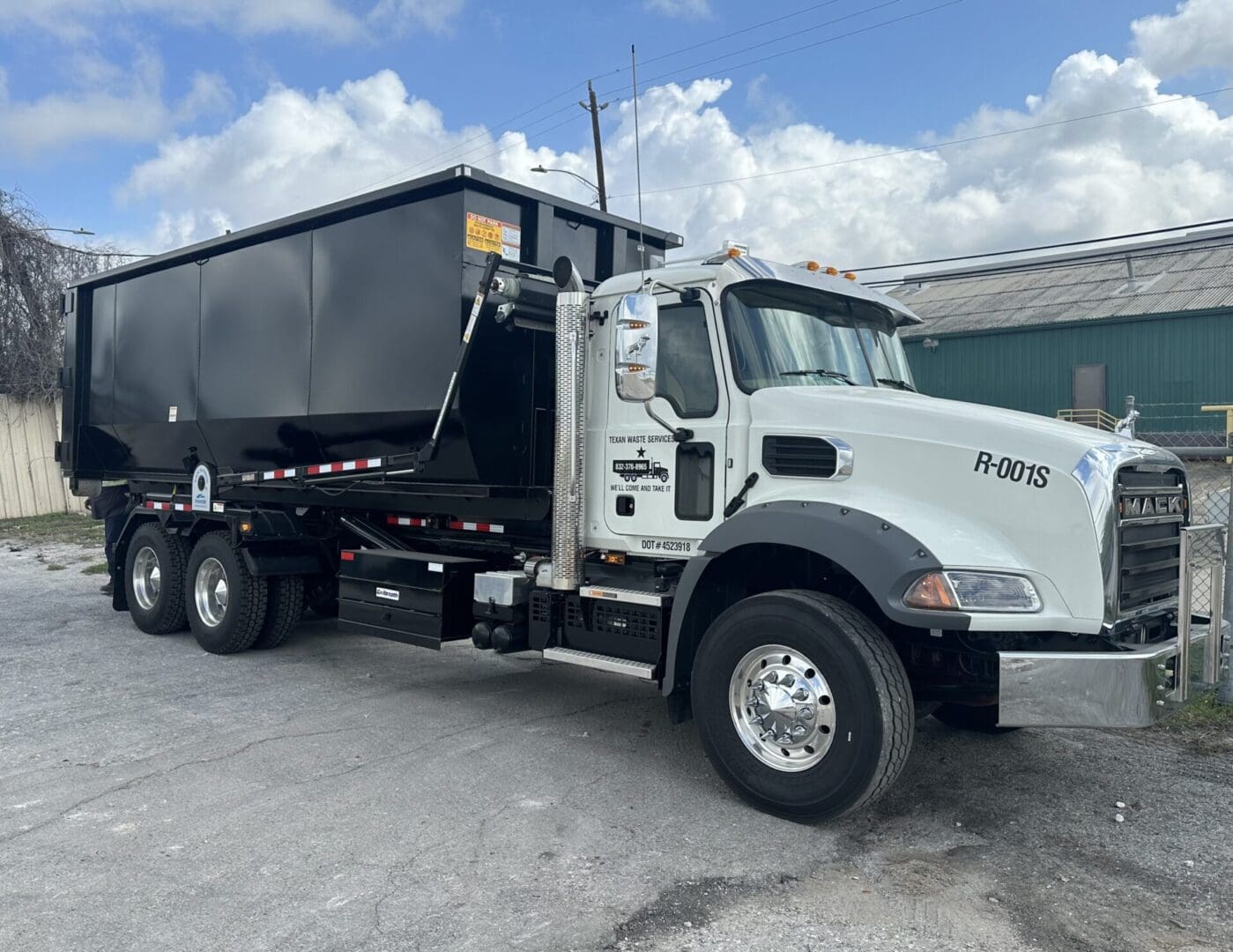 White dump truck with a black container parked on gravel under a cloudy sky.