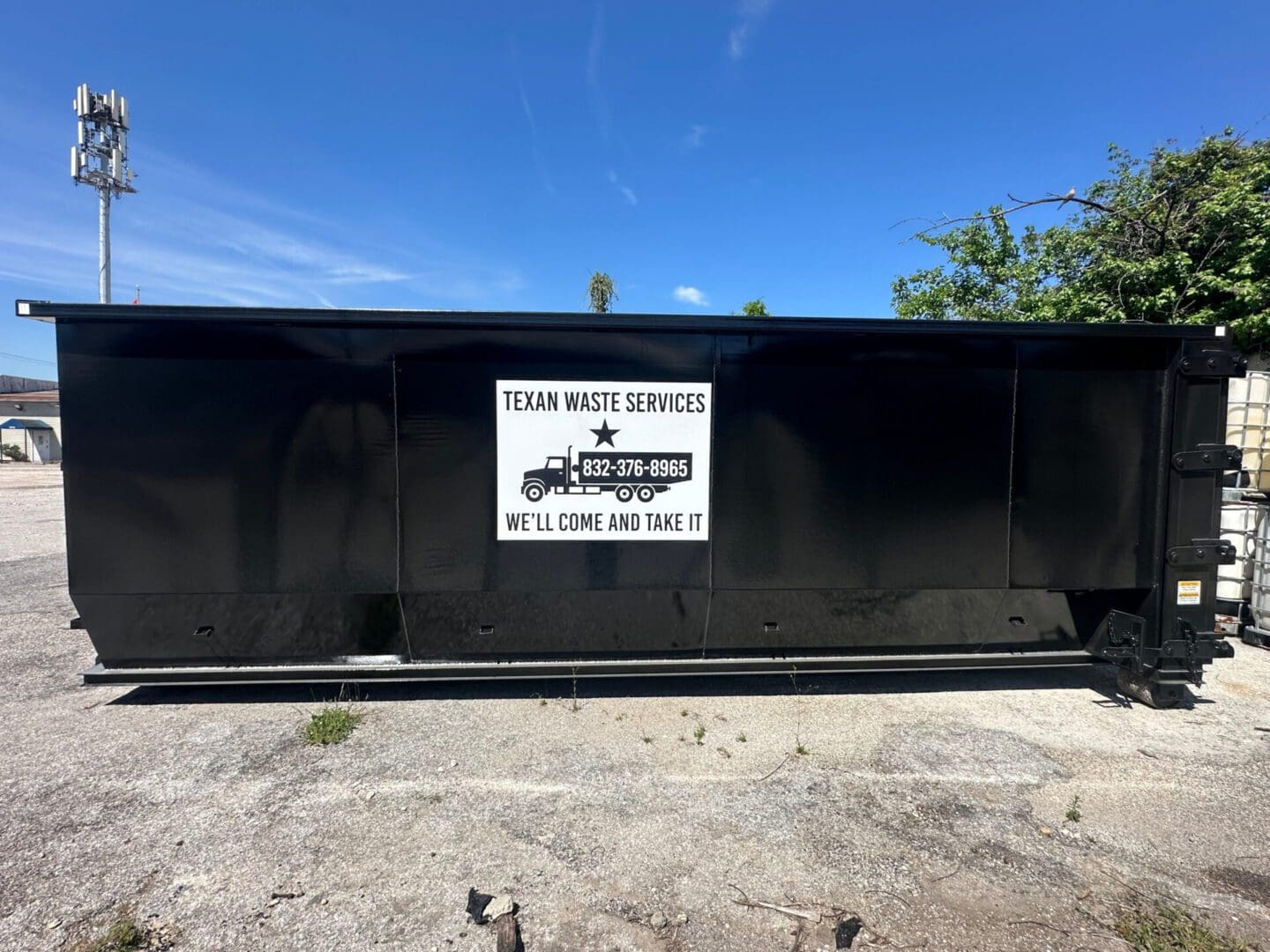 A large black dumpster with a white sign for Tom Metz Hauling and Dumpsters.